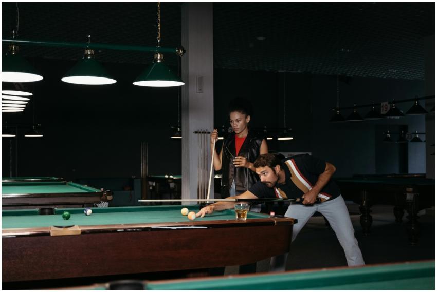 Two adults playing billiards indoors with focus an