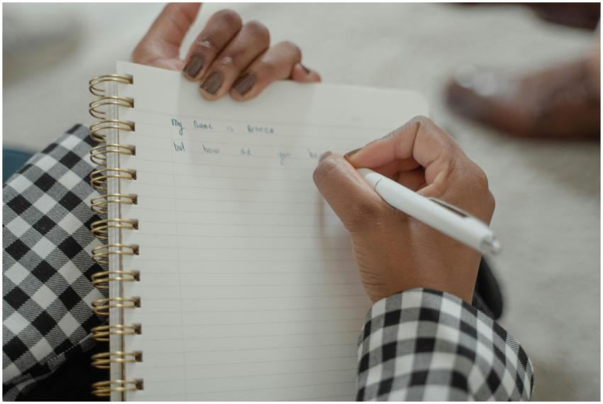 A person writing with a pen on a spiral notebook,