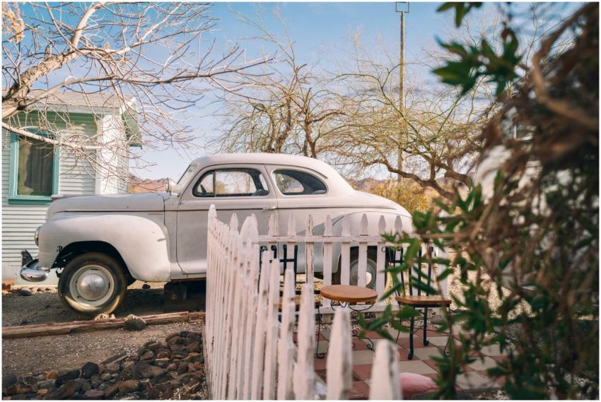 A classic car parked beside a rustic house under a