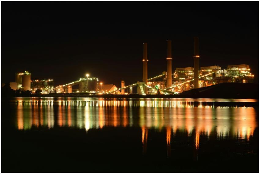 A brightly lit industrial plant reflected in a riv