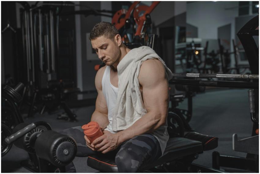 Muscular man sits in gym holding protein shaker af