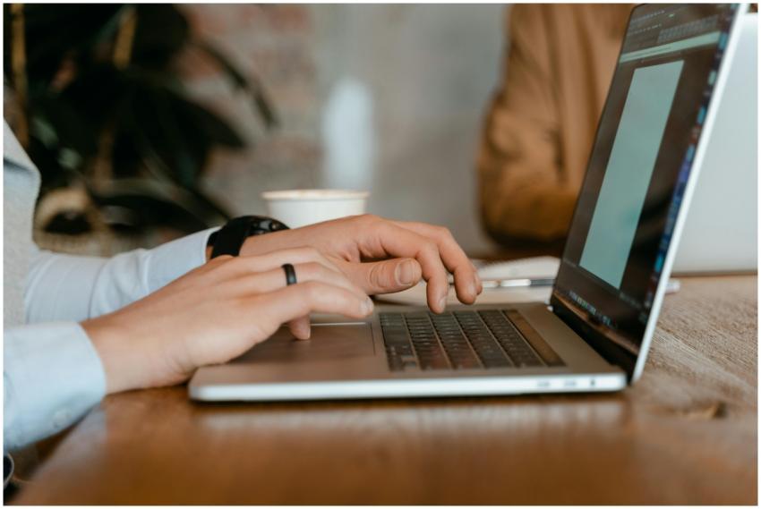 A person typing on a laptop at a wooden table in a
