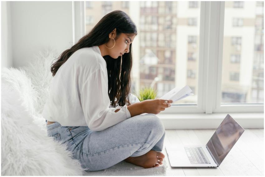 A young woman sits by a window reading documents w