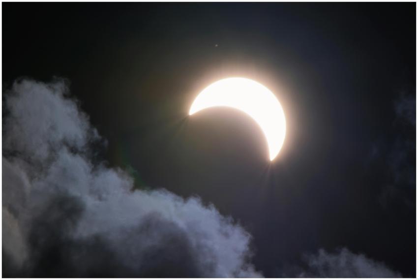 A bright crescent moon partially hidden by clouds