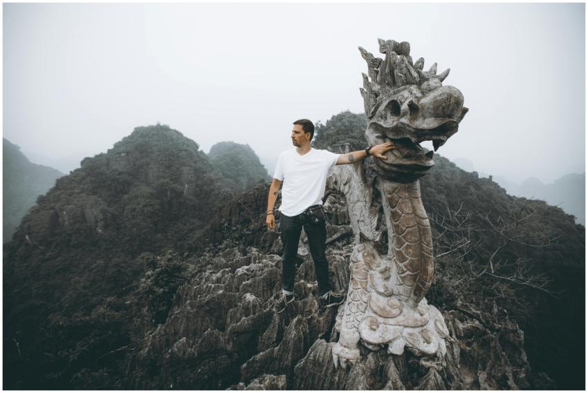 Man poses with a dragon sculpture atop Mua Cave, a