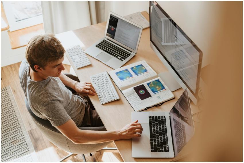 A man multitasks with laptops and a desktop, codin