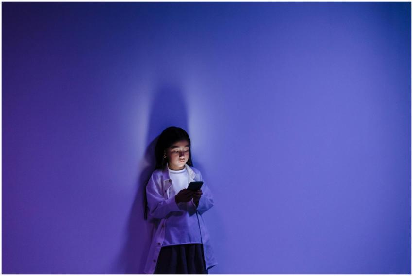 A girl standing against a blue-lit wall engrossed