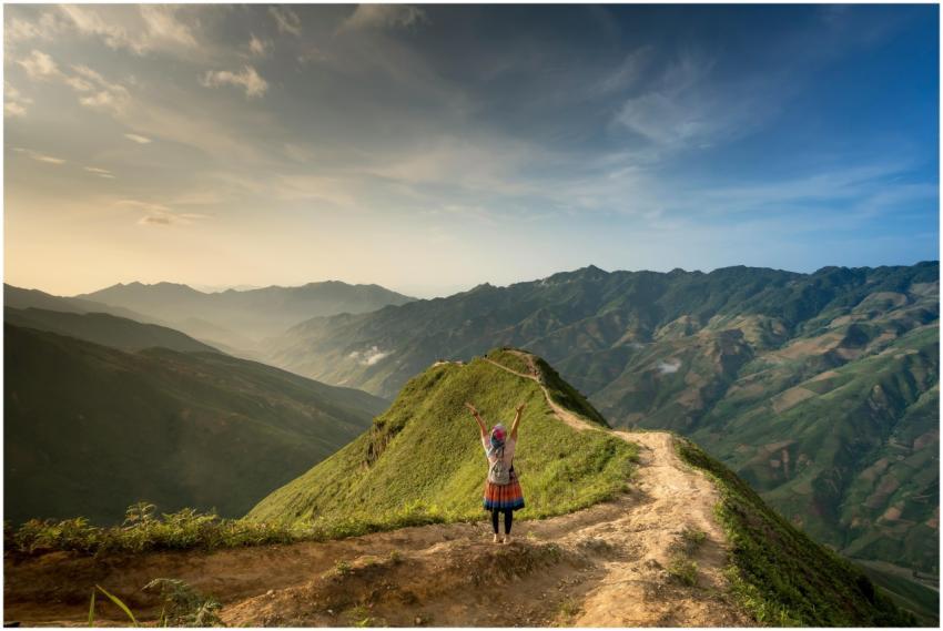 A hiker raises arms in joy on a mountain ridge, ba