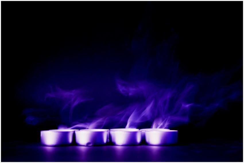 Purple smoke swirls over a row of tealights agains
