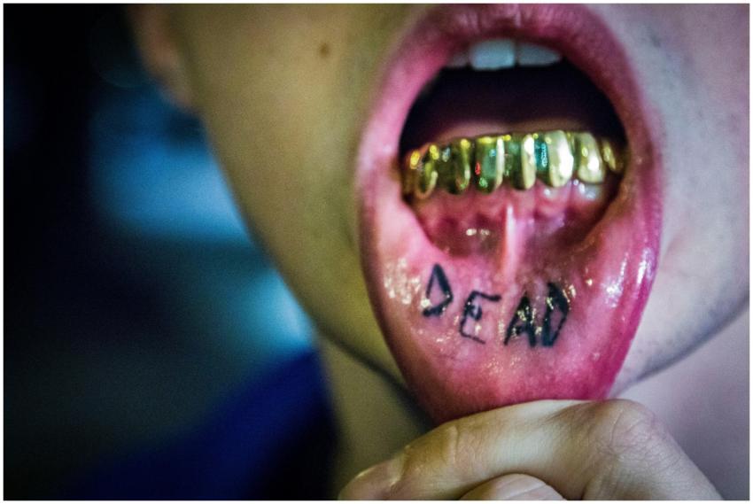 Intense close-up of gold grills and a tattooed ton