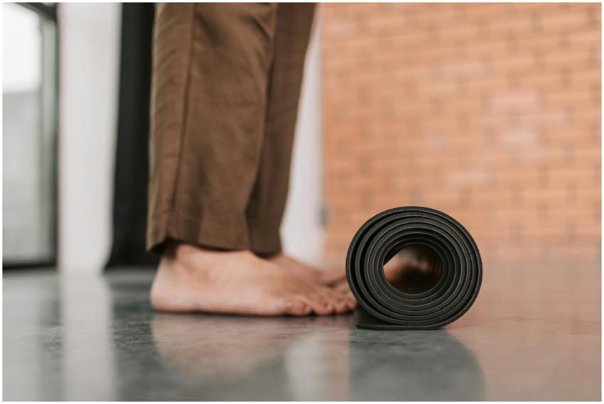 A person standing barefoot by a rolled yoga mat in