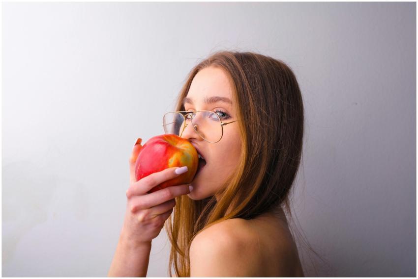 A young woman in glasses takes a bite of a fresh r