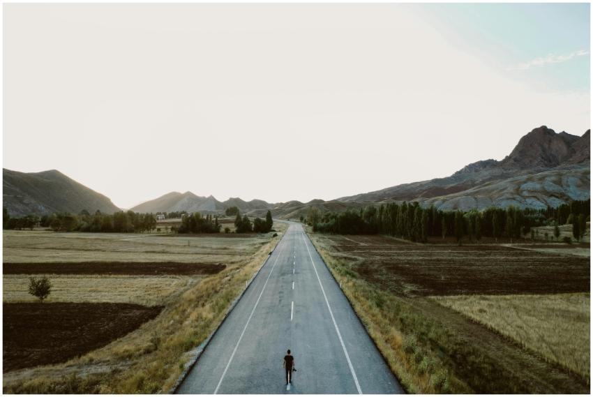 A lone person walks on a rural highway surrounded