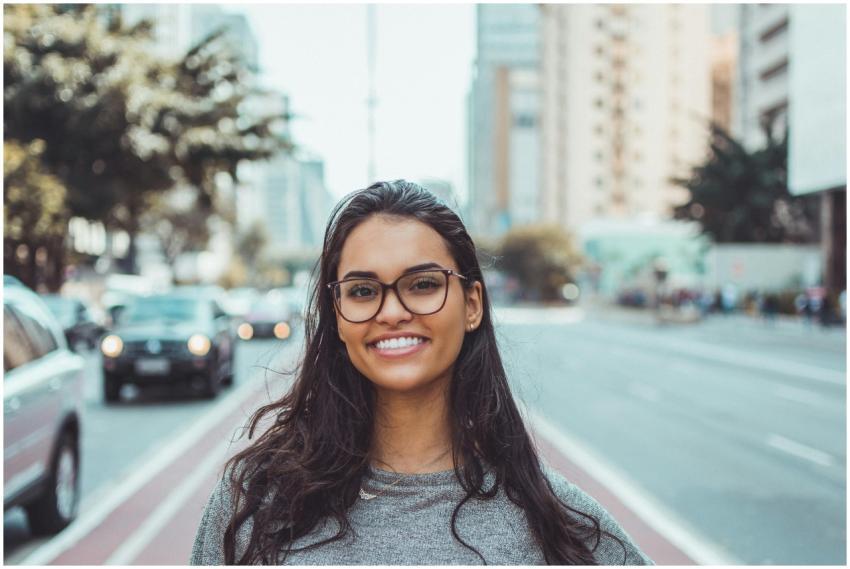 A young woman with glasses smiling on a city stree