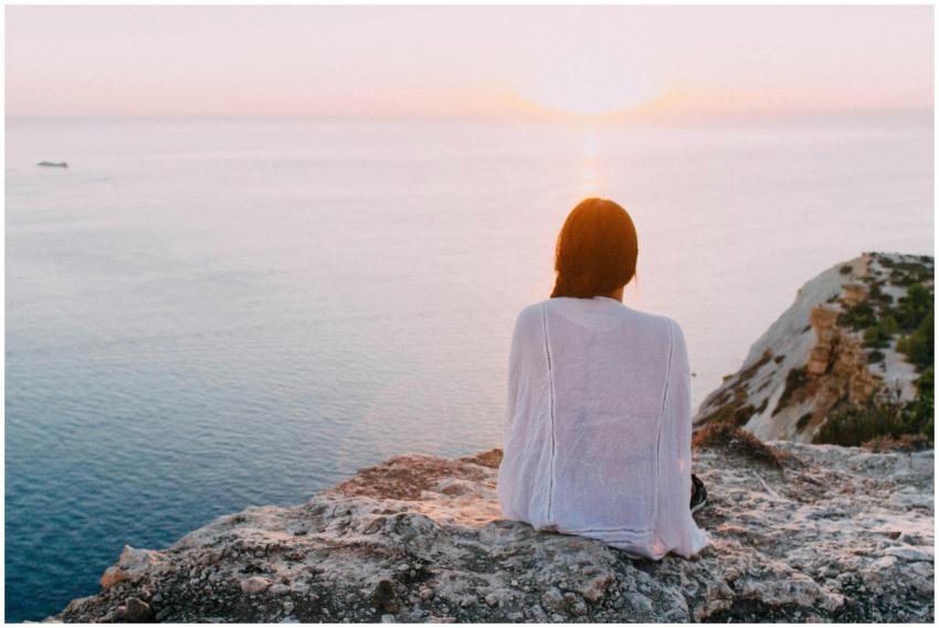 A serene view of a woman sitting on a rocky cliff,