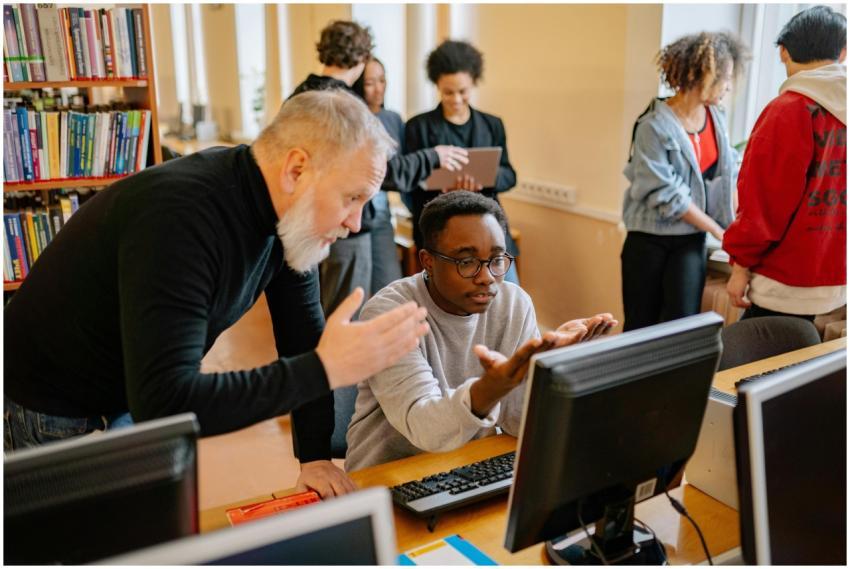 Teacher helping a student at a computer in a busy