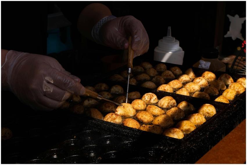 Hands turning takoyaki balls on a hot griddle at a