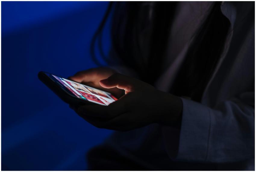 A teenager browses a smartphone in a dimly lit roo