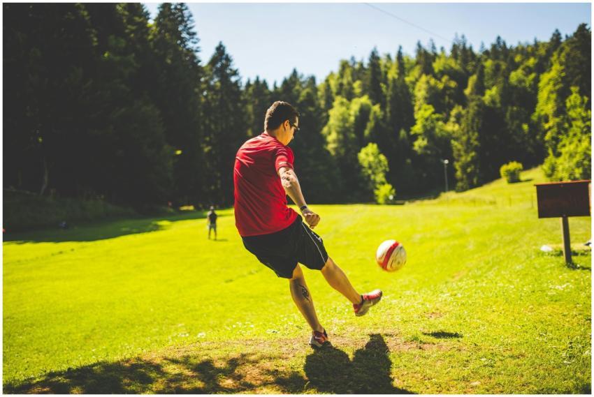 Man in a red shirt kicking soccer ball on sunny da
