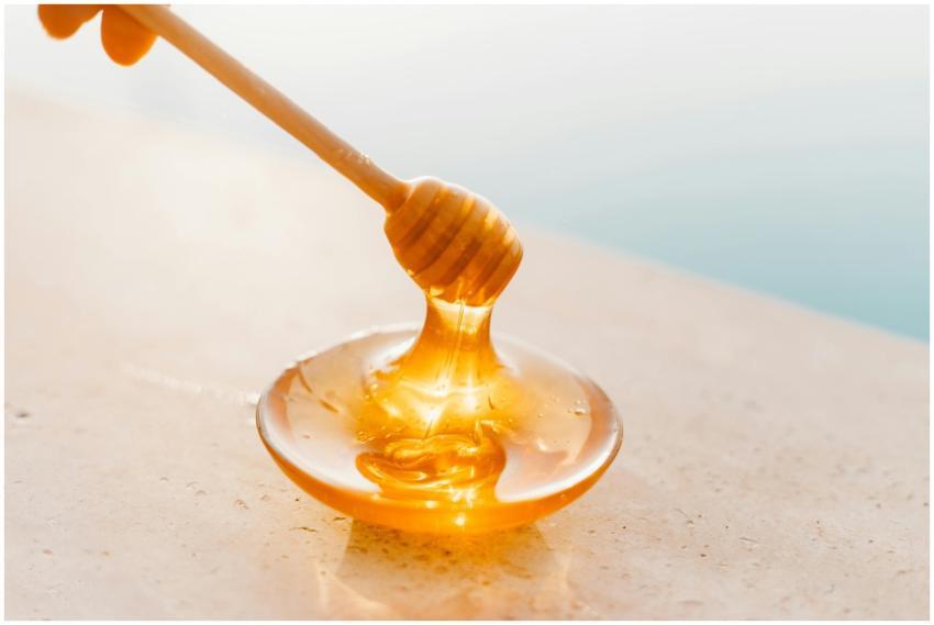 Golden honey flowing from a wooden dipper onto a g