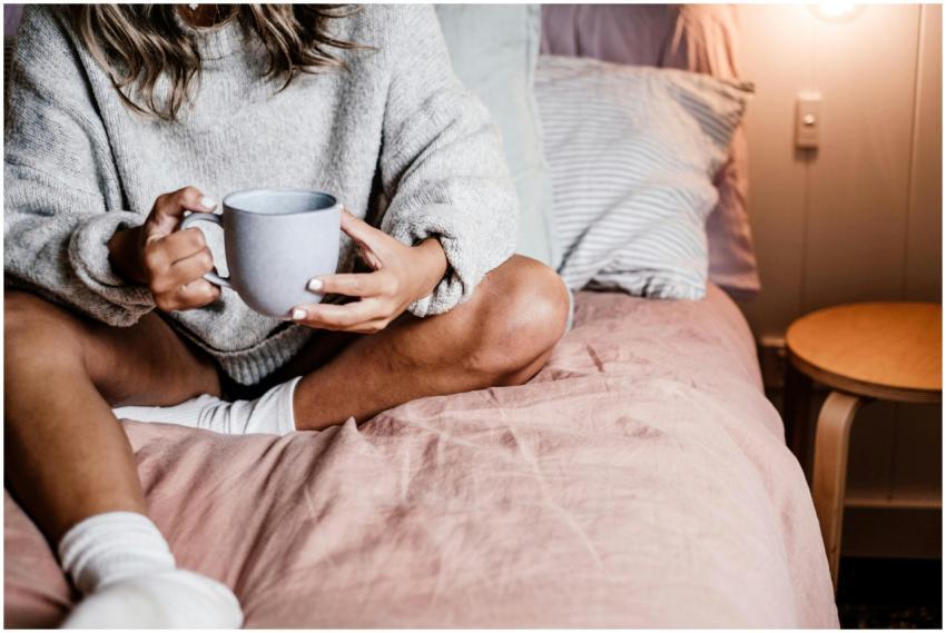 A woman enjoys a warm drink in bed, wearing a cozy