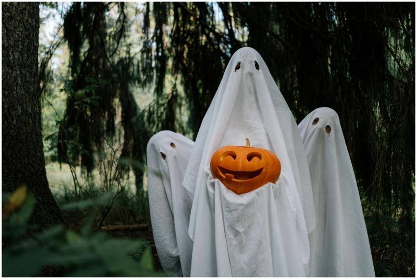 Three ghostly figures holding a carved pumpkin in