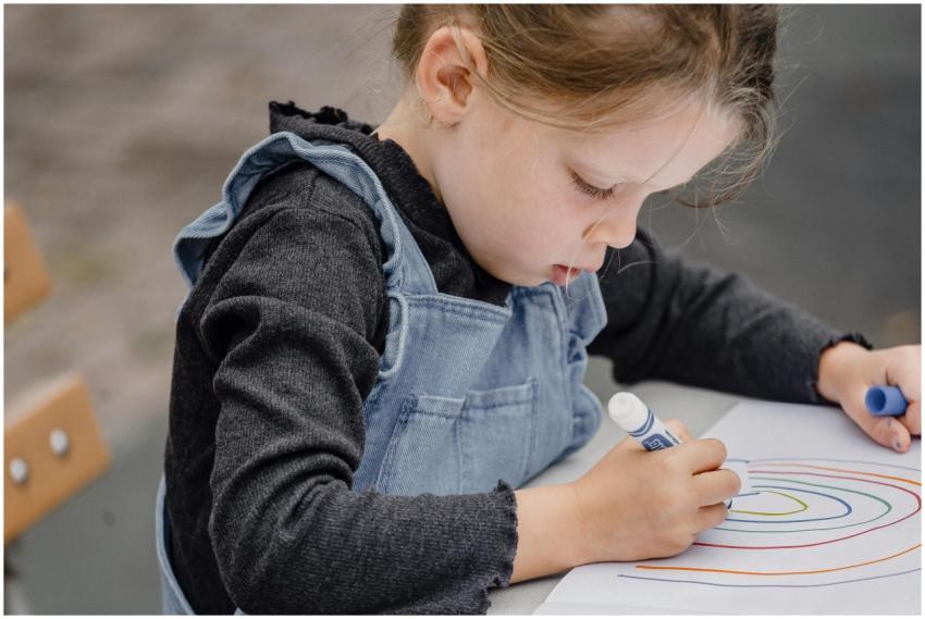 Crop kid sitting on wooden bench at table and hold