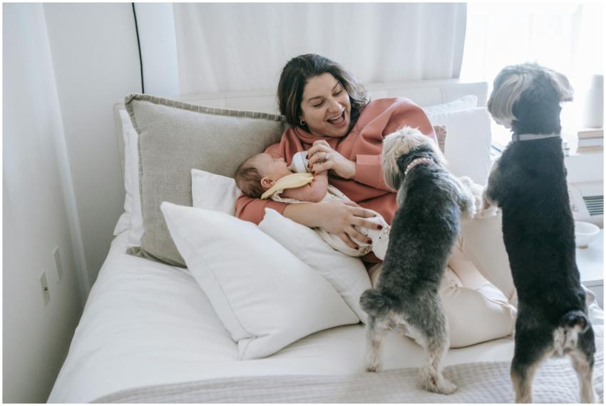 Happy mother feeding baby on bed surrounded by pla