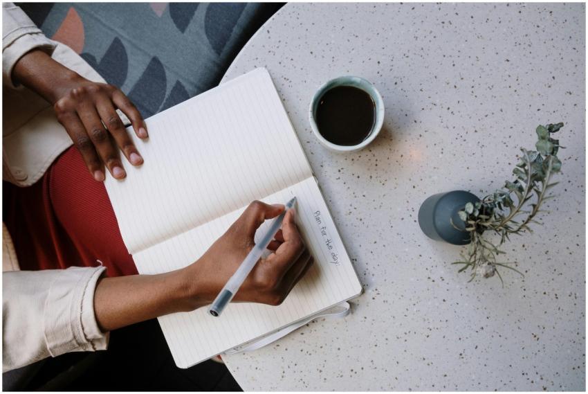 Person writing in a planner with coffee at a café,