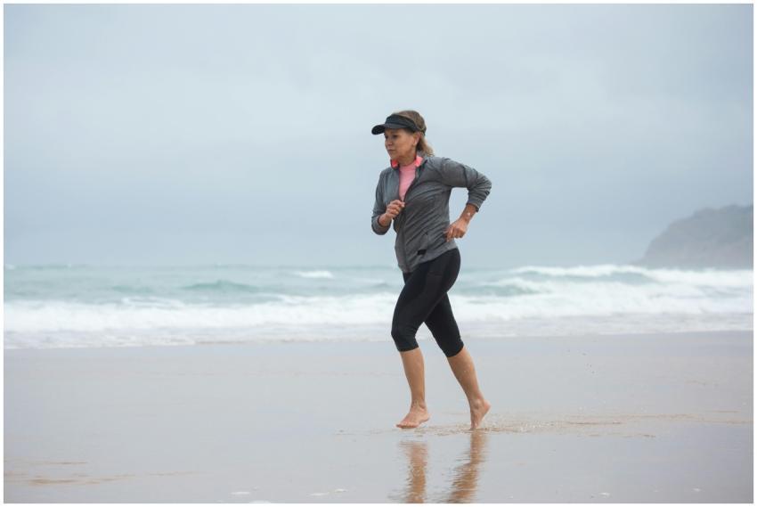 Elderly woman jogging along a sandy beach in Portu