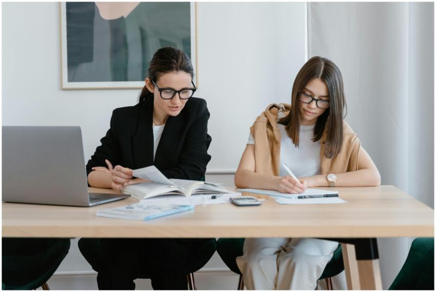 Two women working together with books and a laptop