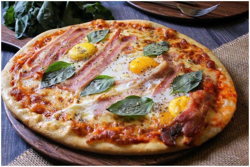 Tasty pizza topped with ham, egg yolks, and fresh