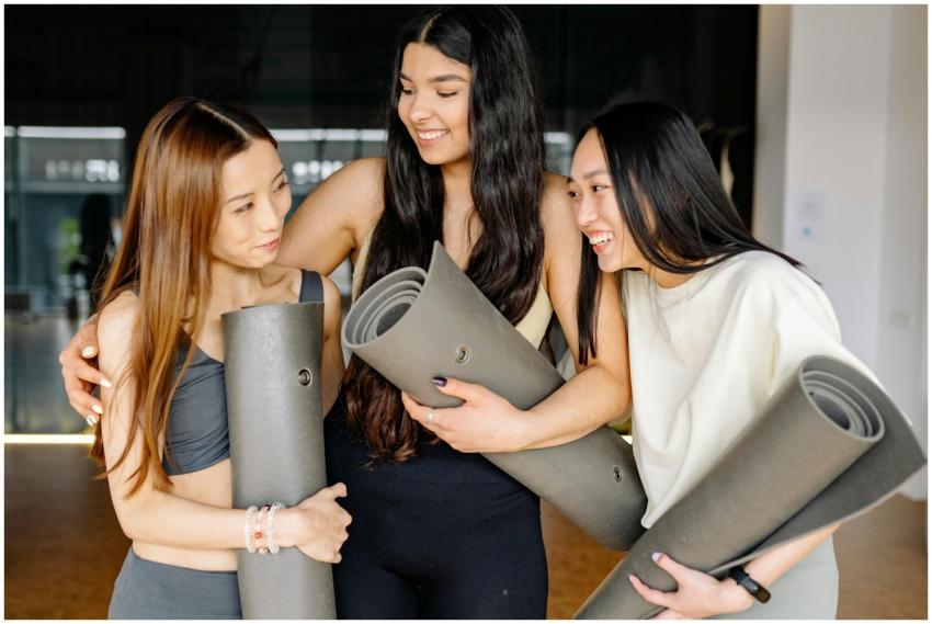 Three women smiling and holding yoga mats during a