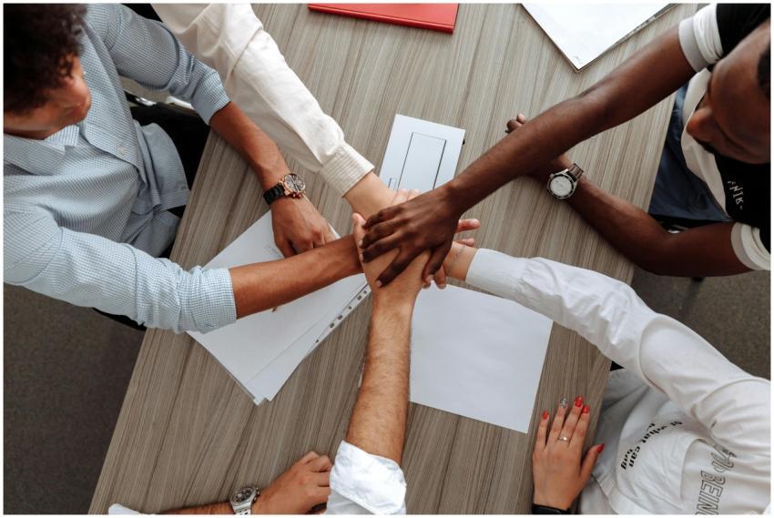 A diverse group of adults join hands in an office,