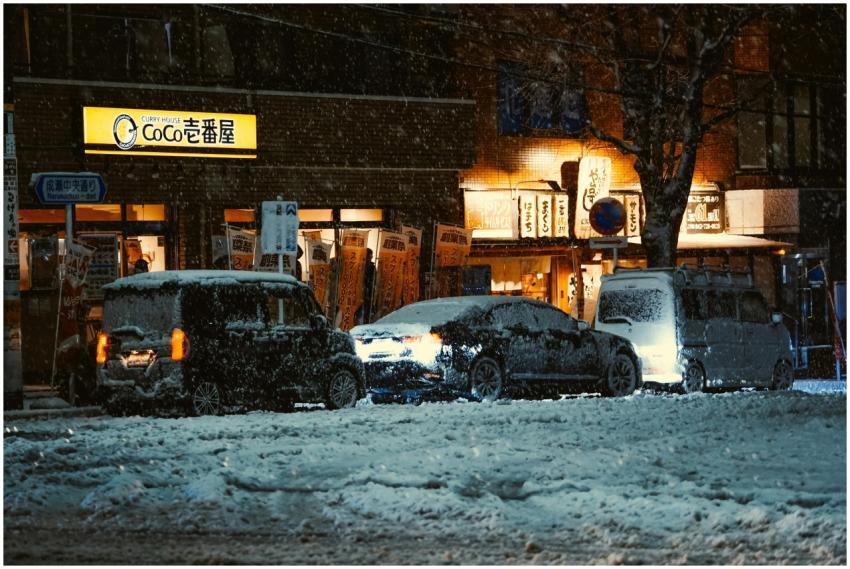 Snow-covered cars outside a lit Tokyo restaurant a