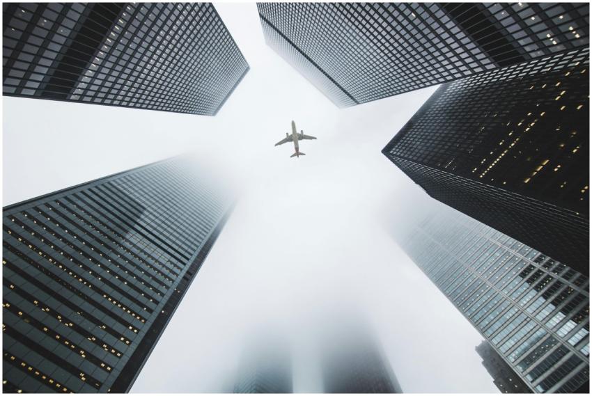 Airplane soaring above fog-enshrouded skyscrapers