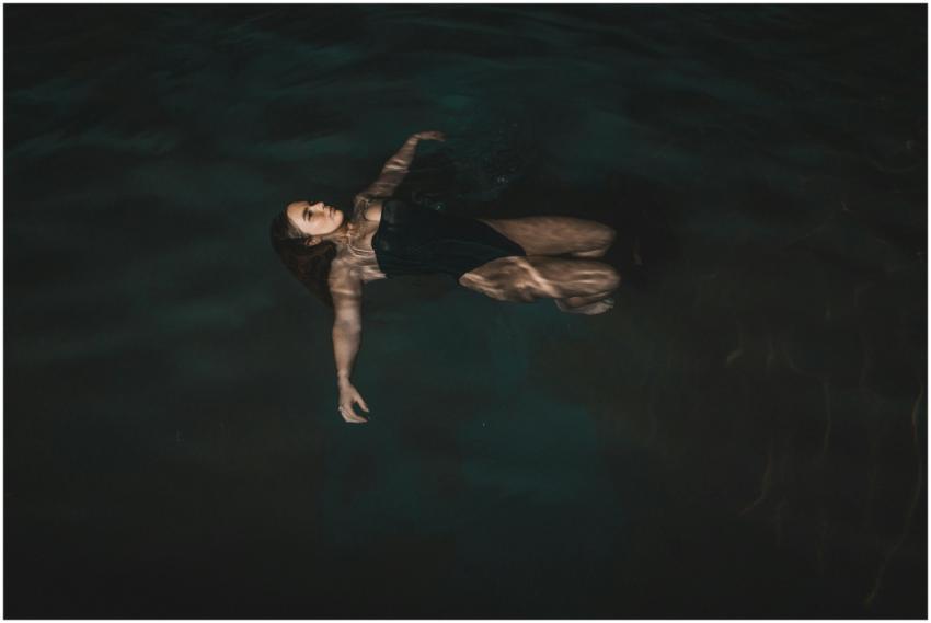 A woman peacefully floats on her back in a dark, s