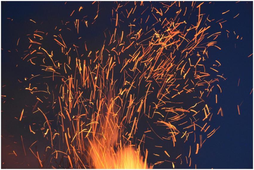 Vibrant orange sparks fly from a fire against a da