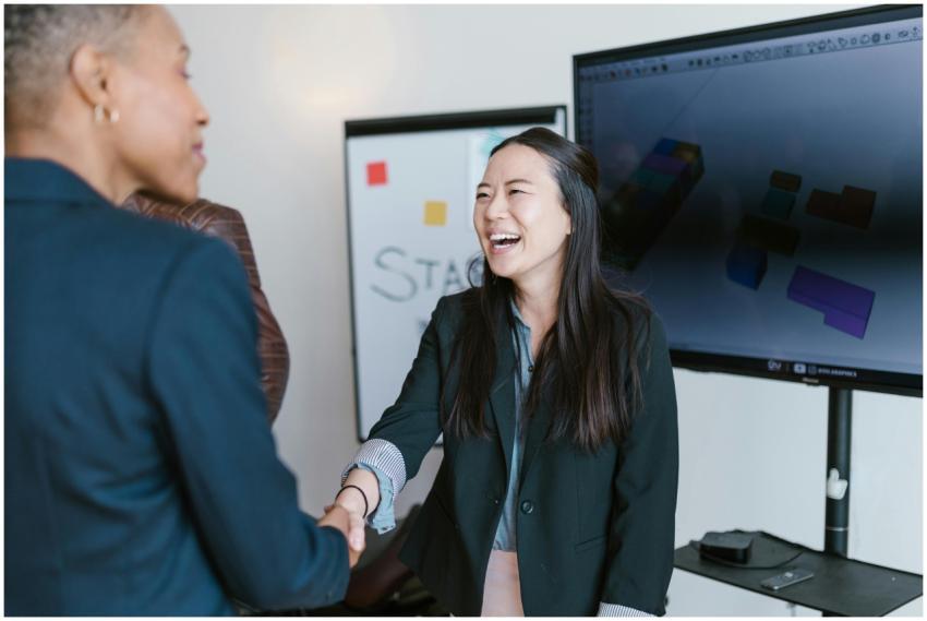 Two businesswomen shake hands while smiling in a m