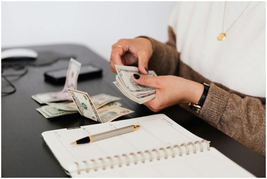 Close-up of person counting cash with notepad on d