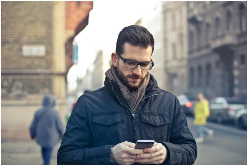 Adult man with glasses using a smartphone on a cit