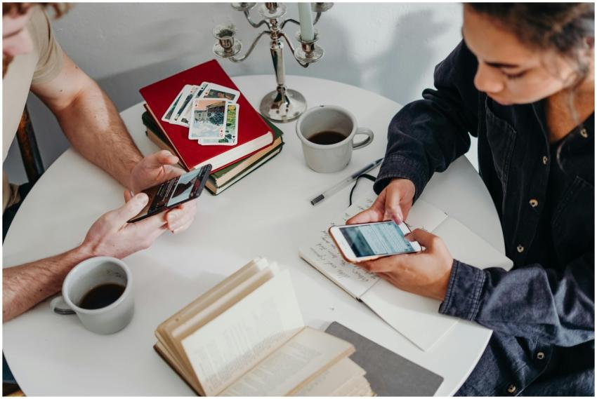 A couple texting with coffee and books at a home t