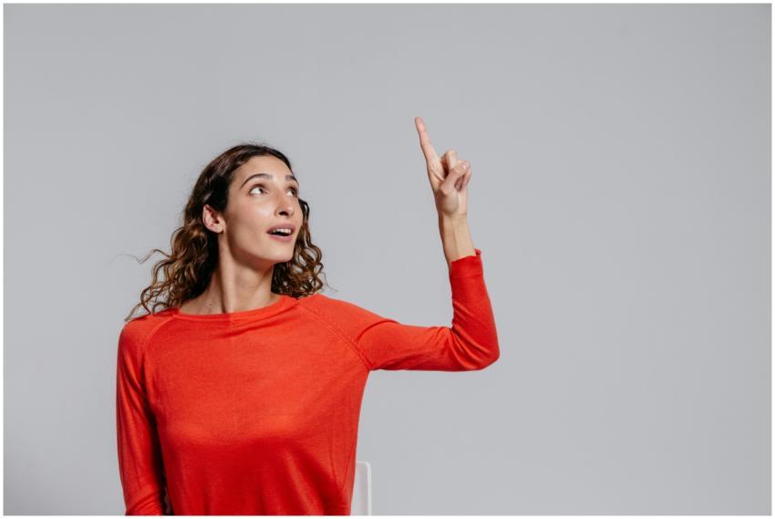 Portrait of a woman in red pointing upwards agains