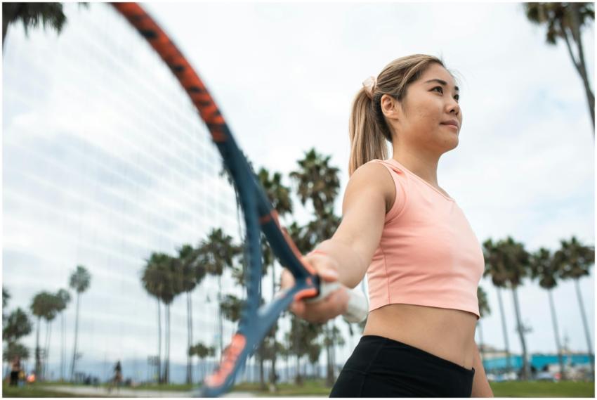 Active woman playing tennis in park with palm tree