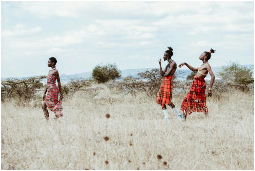 Three women in traditional attire walk across a sa