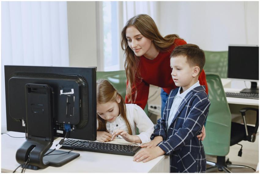 A teacher guides two children using a computer in