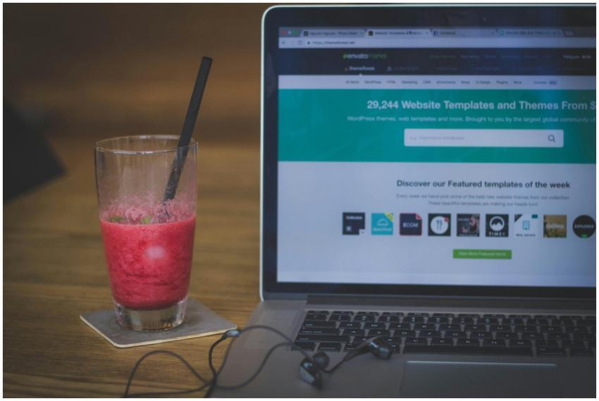 A fruit shake on a desk next to a laptop displayin
