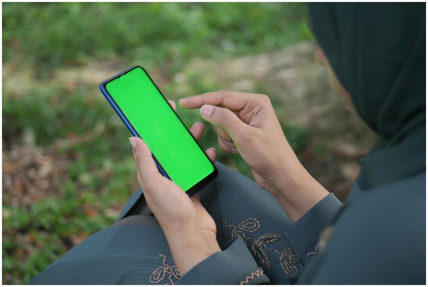 Person holding smartphone with green screen in a n