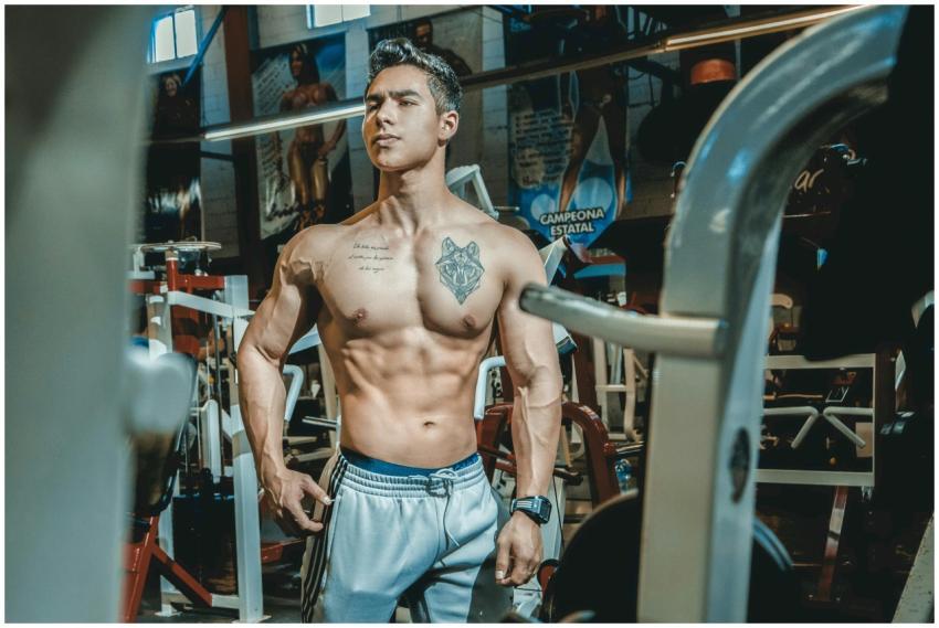 Shirtless man with tattoos posing in a gym environ