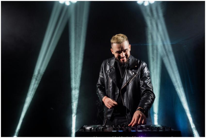 A DJ in a black leather jacket mixing music under